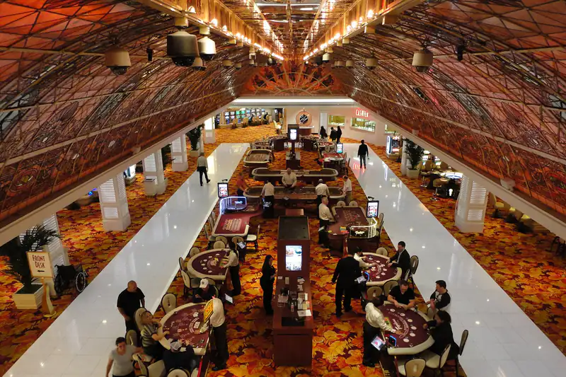 A high view of a casino floor with rows of table games under a patterned ceiling