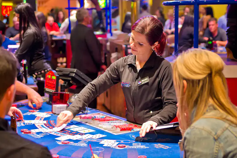 A smiling female dealer dealing cards to players at a blue blackjack table