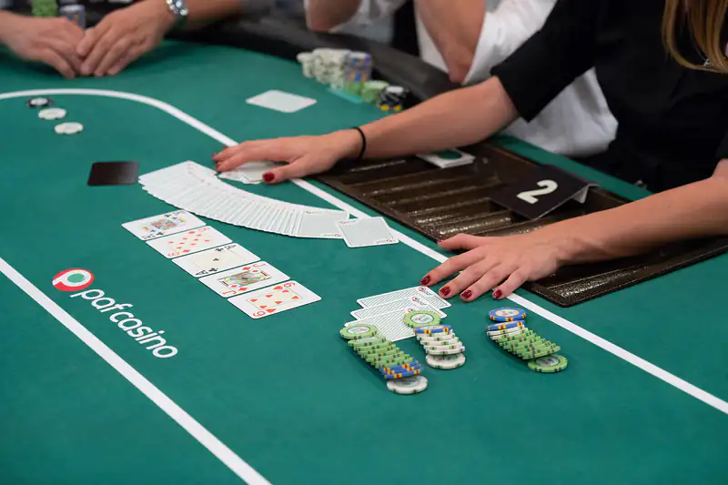 A dealer spreading cards on a green poker table beside chip stacks